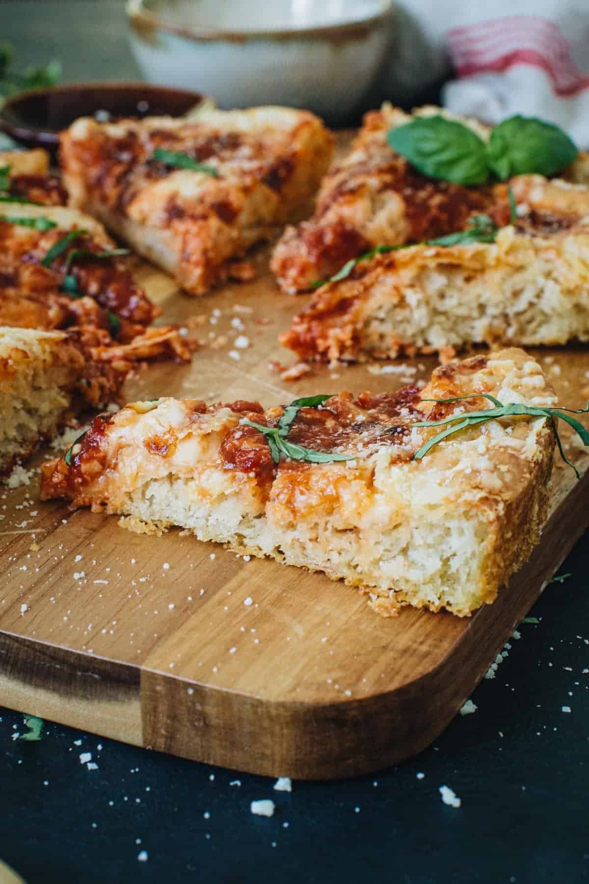 Slice of cast iron skillet pizza on a wooden cutting board.