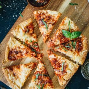 Cast iron skillet pizza sliced on a wooden cutting board.