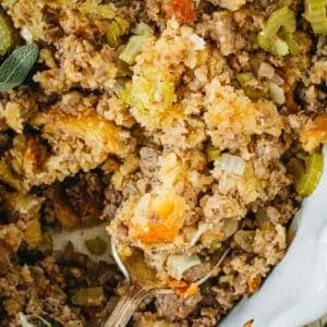 Sausage dressing in a white baking dish with a silver spoon.