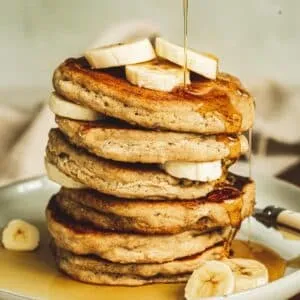 Vegan banana pancakes stacked with syrup dripping down the side.