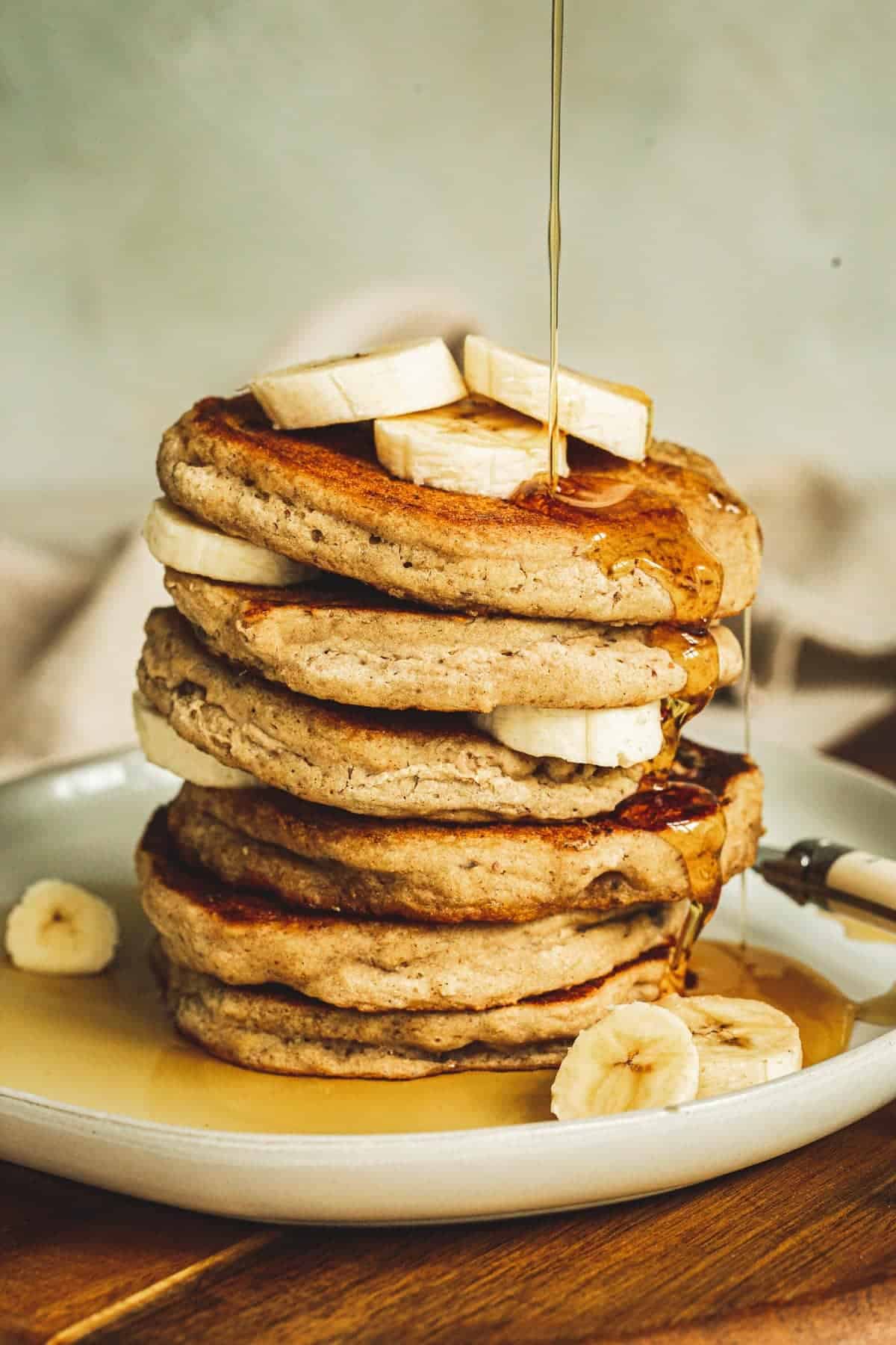 Vegan banana pancakes stacked with syrup dripping down the side.