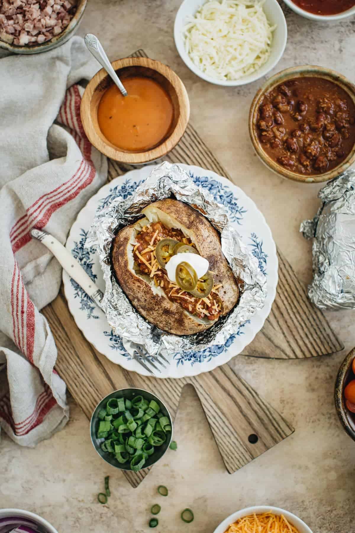 Baked potato bar with a loaded potato in the center on a blue and white plate.