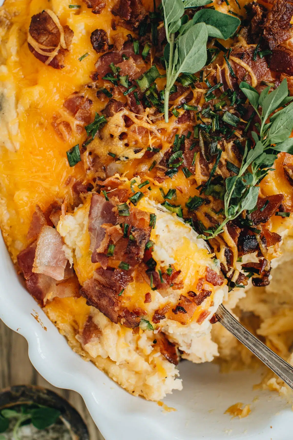 Loaded mashed potato casserole in a white casserole dish with a silver spoon scooping some out.