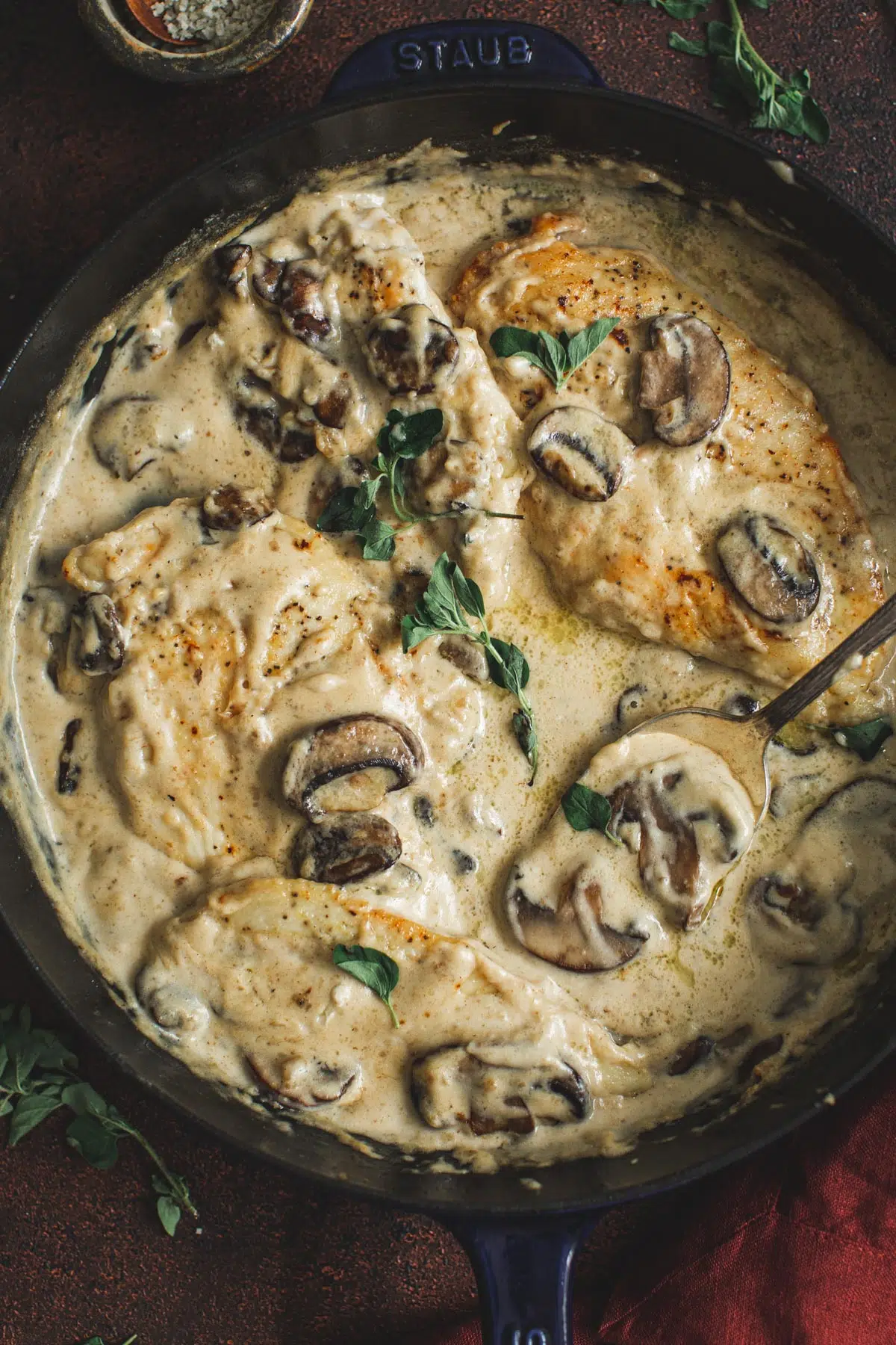 Cream of mushroom chicken in a skillet topped with fresh oregano.