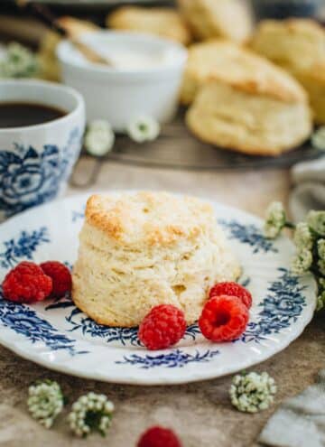 English scones on a blue and white plate with fresh raspberries around it.