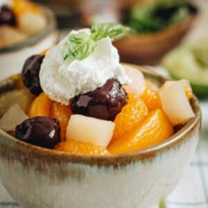 Fruit cocktail in a bowl topped with whipped cream and fresh basil.