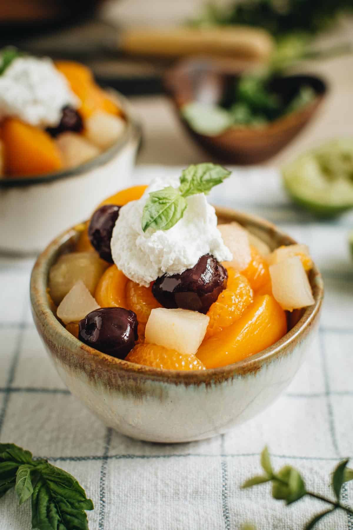 Fruit cocktail salad in a bowl topped with whipped cream and fresh basil.