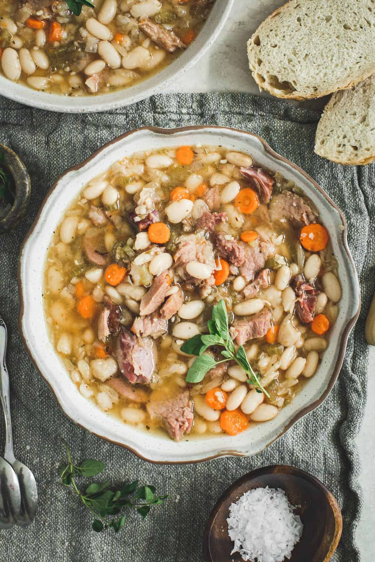 Ham and white bean soup in a bowl with a sprig of fresh oregano on top.