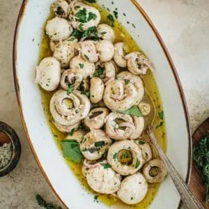 Italian marinated mushrooms in an oval bowl with a silver serving spoon.