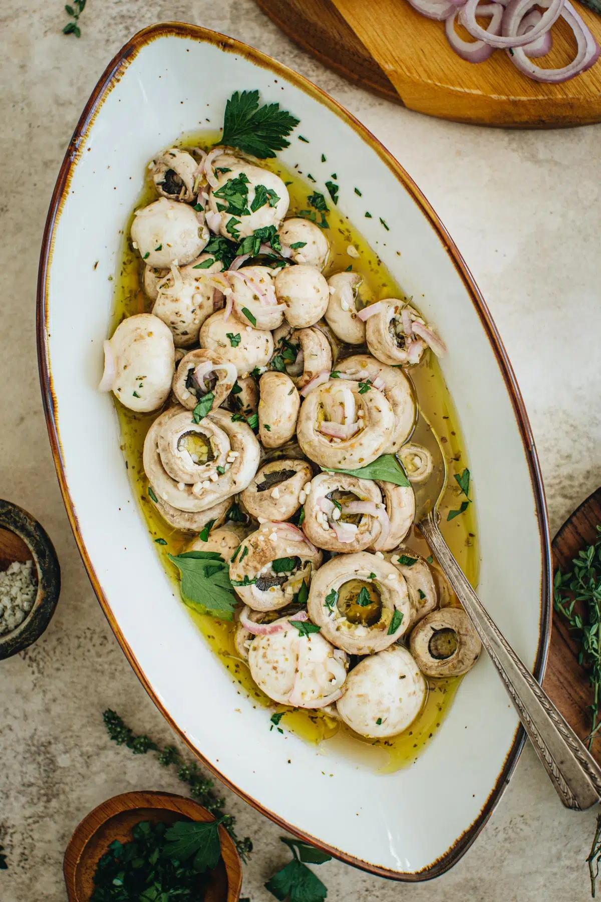 Italian marinated mushrooms in an oval bowl with a silver serving spoon.