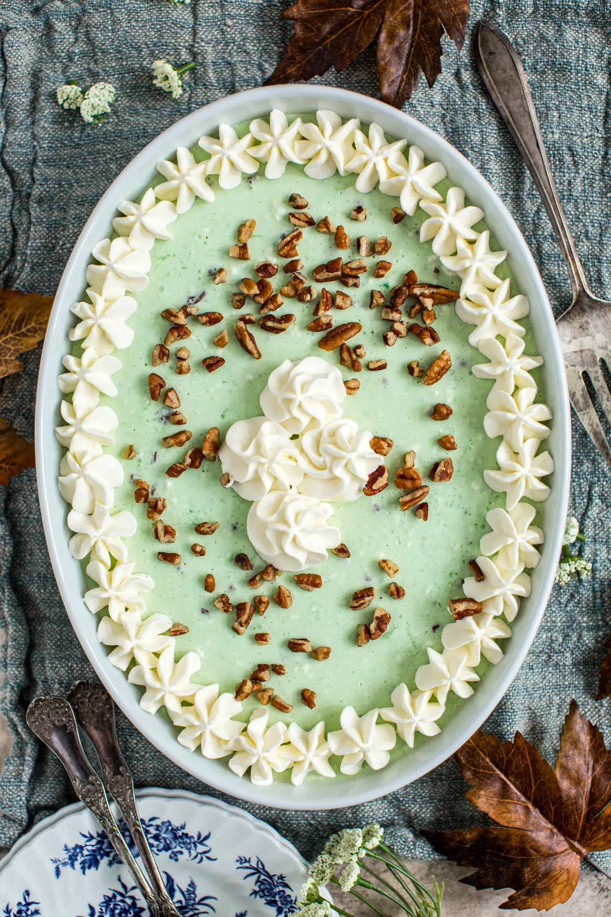 Lime jello salad in an oval casserole dish topped with whipped cream and chopped pecans.