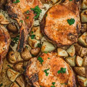Oven baked pork chops and potatoes on a baking sheet.