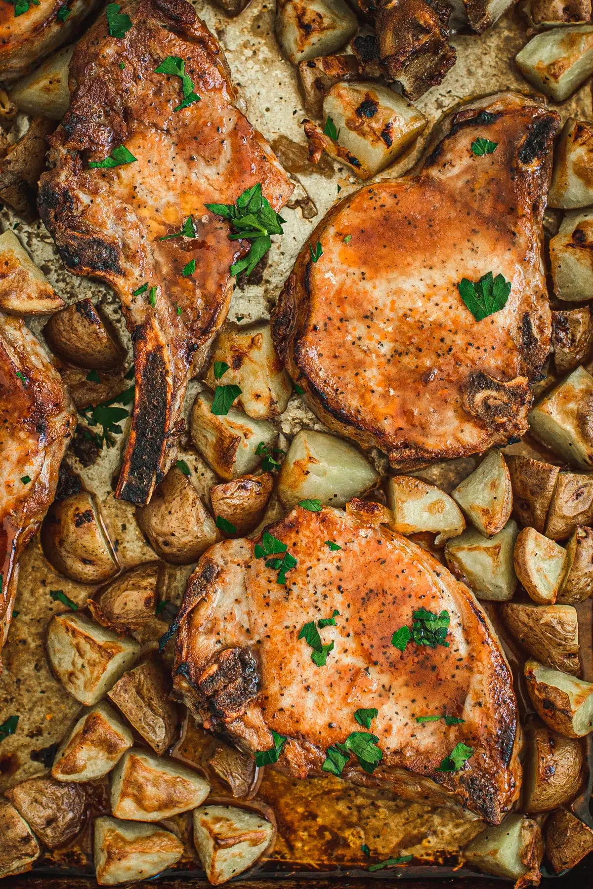 Oven baked pork chops and potatoes on a baking sheet.