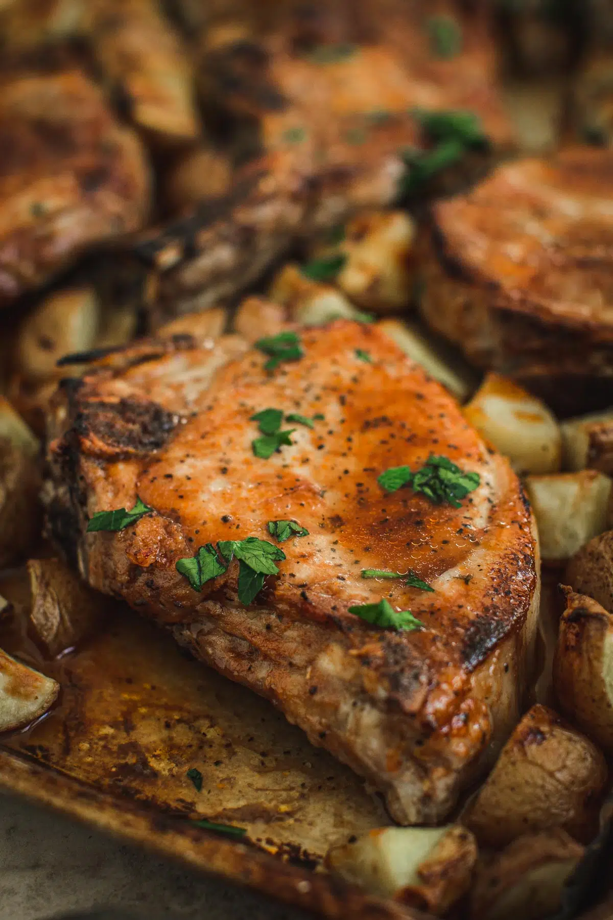 Pork chops and potatoes with fresh parsley sprinkled on top on a baking sheet.