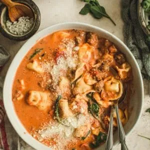 Sausage and tortellini soup in white bowl with two spoons.