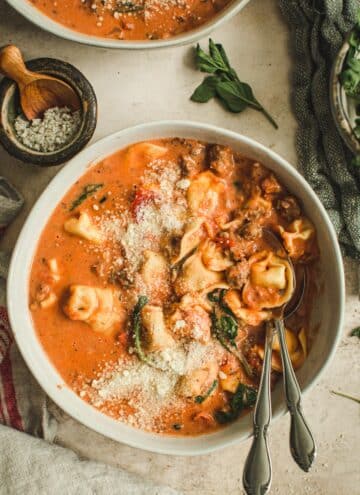 Sausage and tortellini soup in white bowl with two spoons.