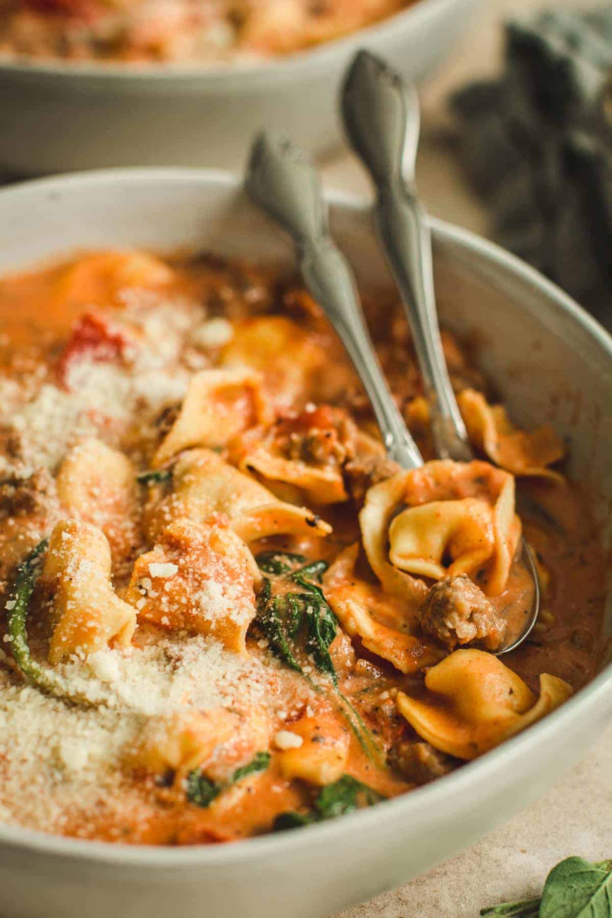 Sausage and tortellini soup with spinach in a bowl with two spoons.