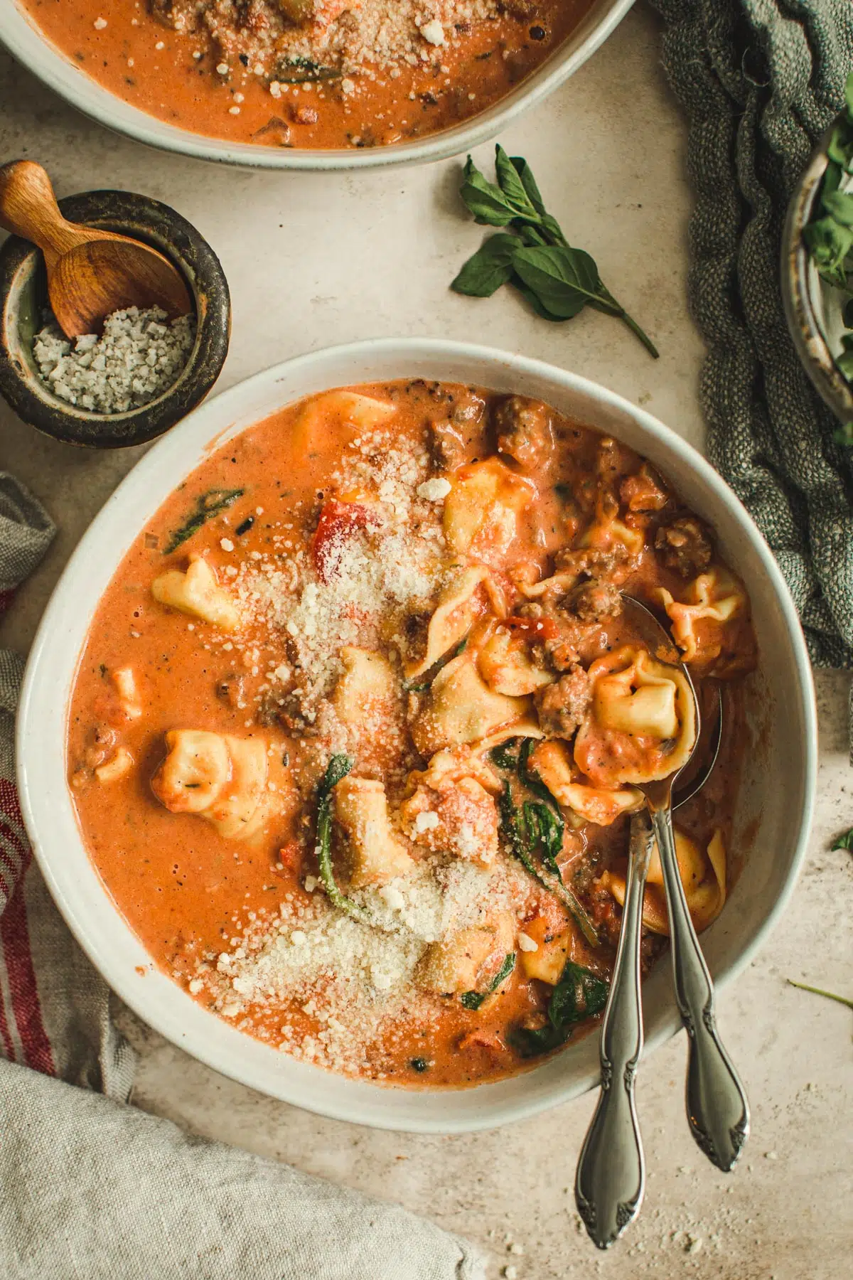 Sausage and tortellini soup topped with parmesan cheese in a bowl with two spoons.