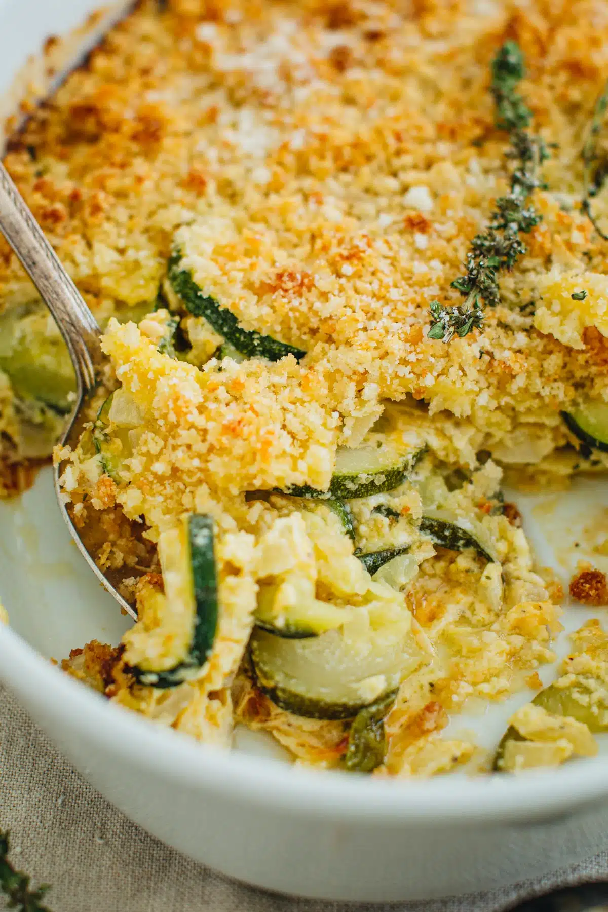 Zucchini casserole on top of a silver serving spoon in a white casserole dish.