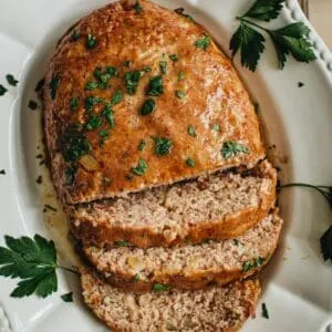 Ham loaf sitting on a platter with half of it sliced.