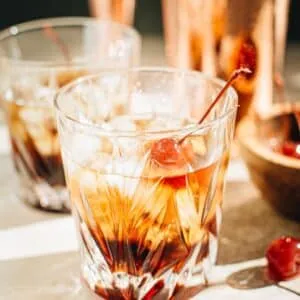 Black Russian in a rock glass with ice and a cherry garnish.