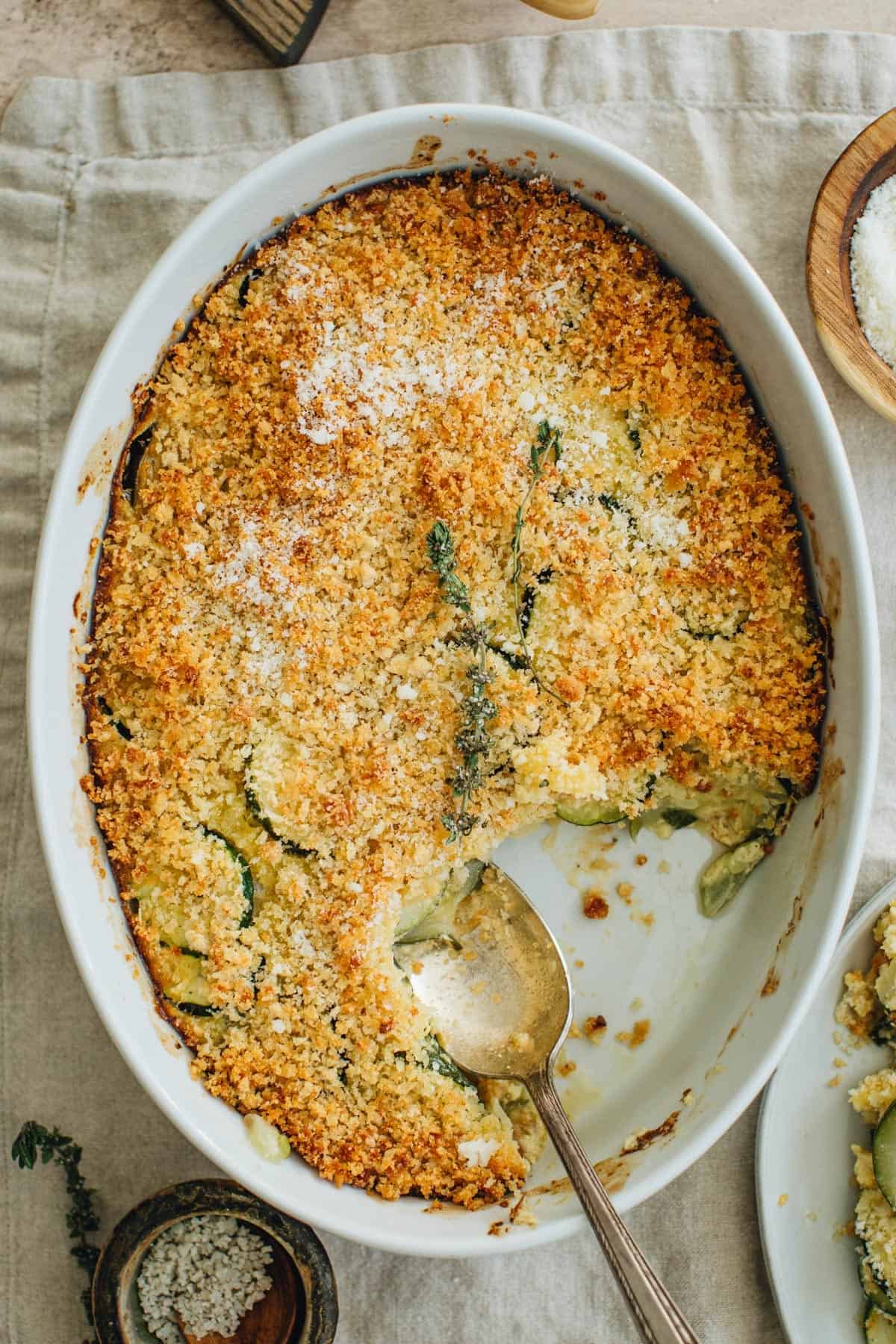 Cheesy zucchini casserole in a white casserole dish with a silver serving spoon.