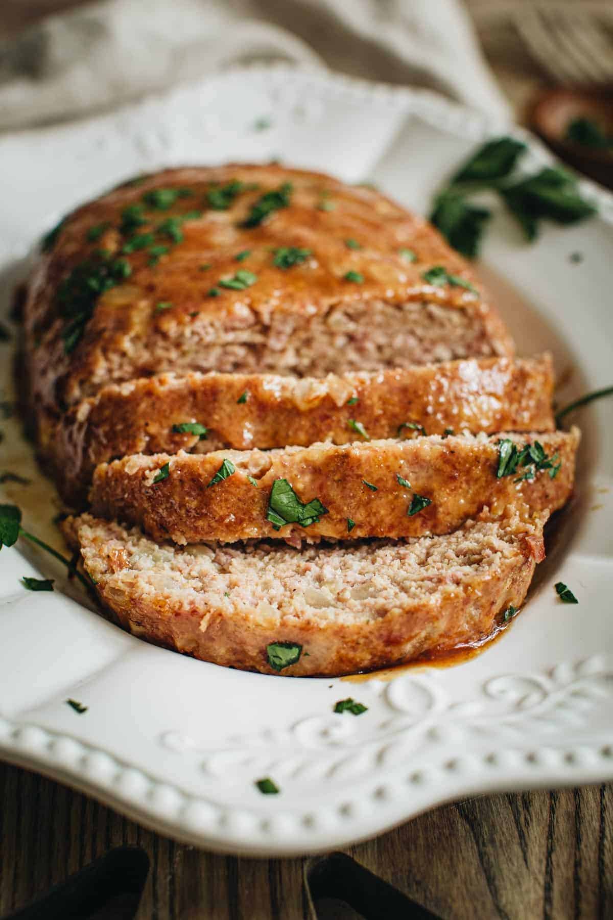 Ham loaf sliced and topped with fresh parsley on a white platter.