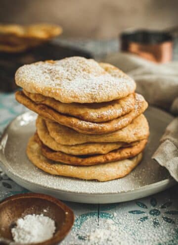 Indian fry bread stacked on a plate and dusted with powdered sugar.