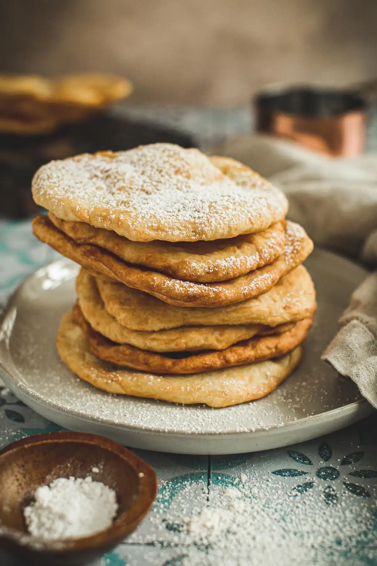 Indian fry bread stacked on a plate and dusted with powdered sugar.