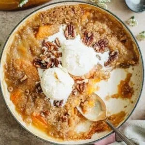 Peach crumble topped with chopped pecans and two scoops of vanilla ice cream.