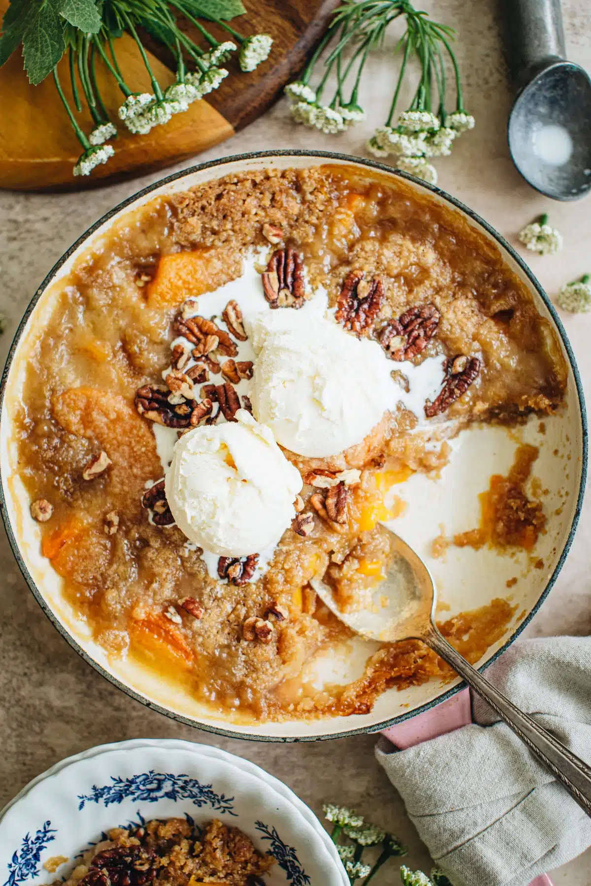 Peach crumble in a pink skillet with vanilla ice cream scoops on top.