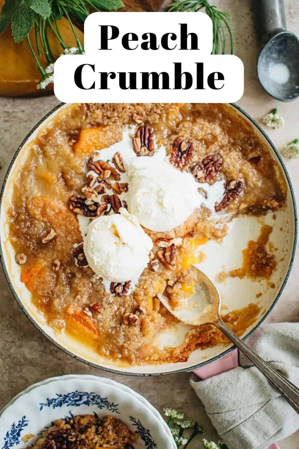 Peach crumble recipe in a pink skillet topped with ice cream.