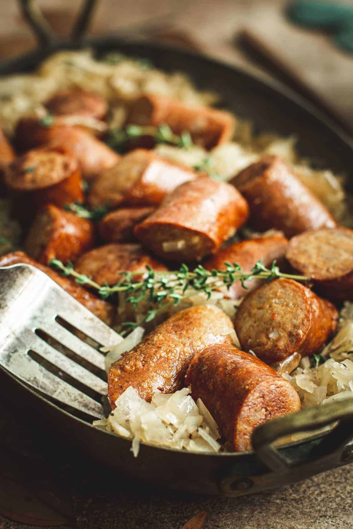 Sauerkraut and sausage in an oval pot with a silver serving fork.