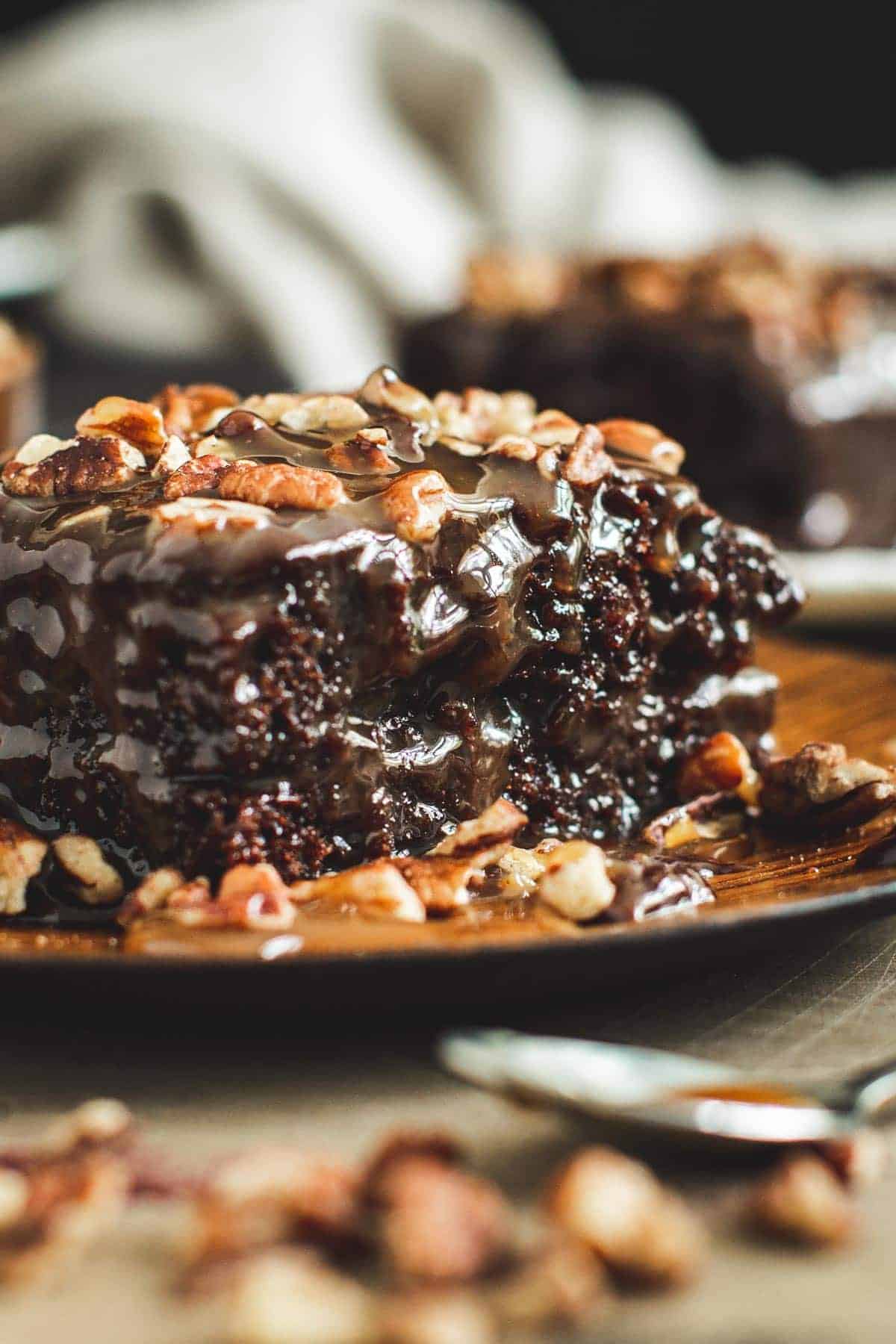 Chocolate turtle cake topped with chopped pecans on a wooden plate.