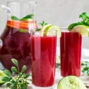 Fruit punch in glasses with a pitcher behind them.