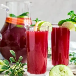 Fruit punch in glasses with a pitcher behind them.