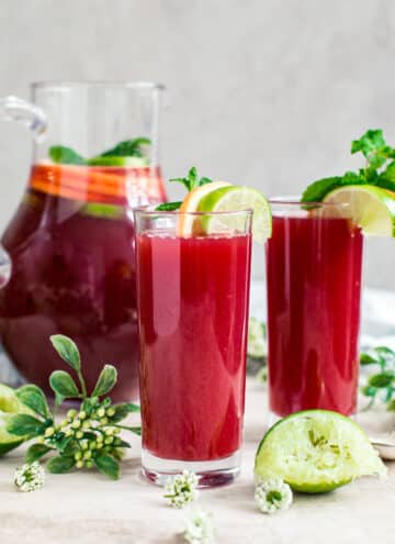 Fruit punch in glasses with a pitcher behind them.