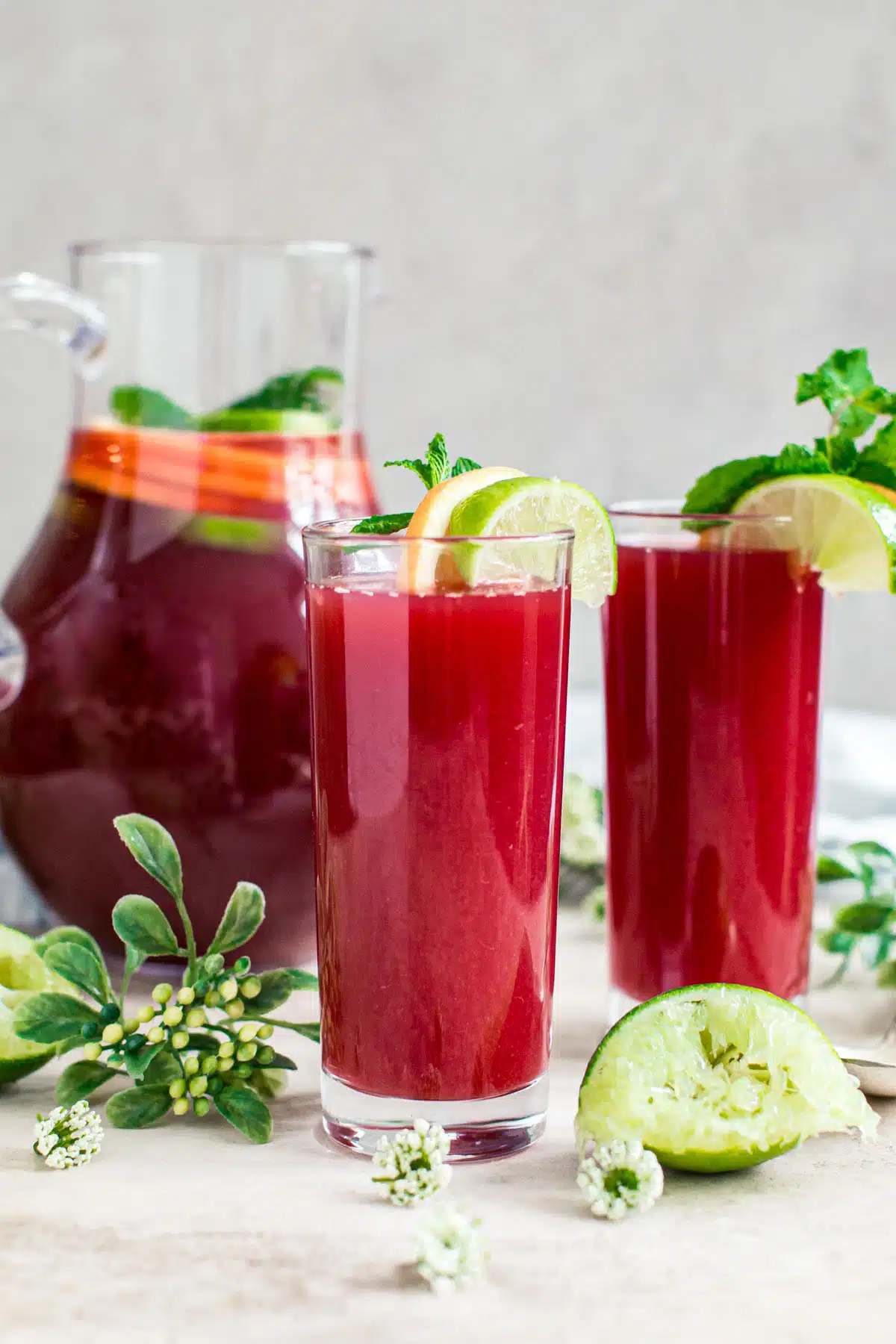 Fruit punch in glasses with a pitcher behind them.