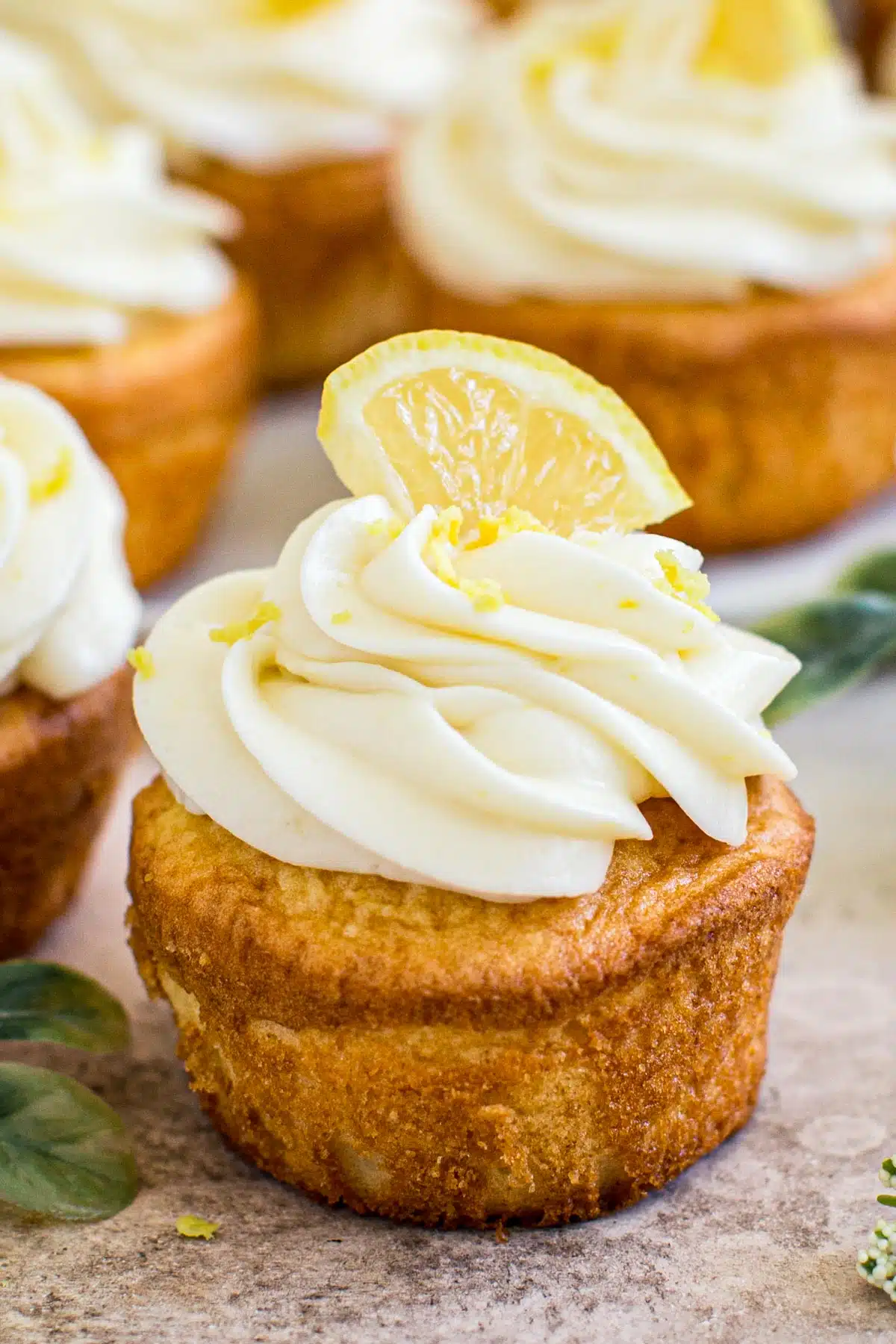 Lemon cream cheese frosting on top of a cupcake topped with lemon zest and a lemon wedge.