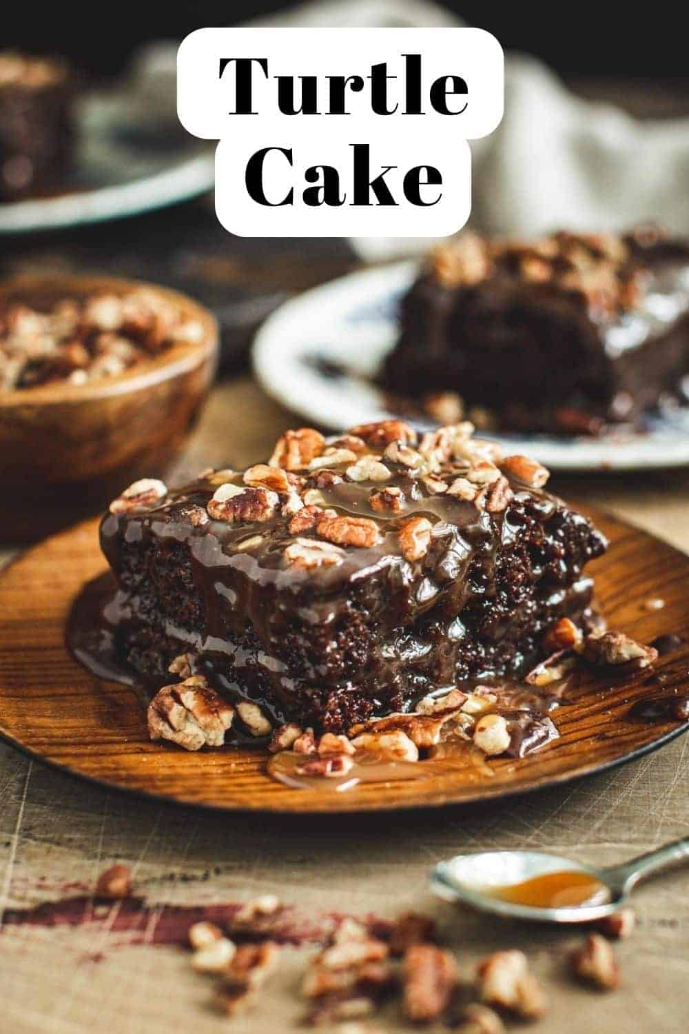 Chocolate turtle cake topped with chopped pecans on a wooden plate.