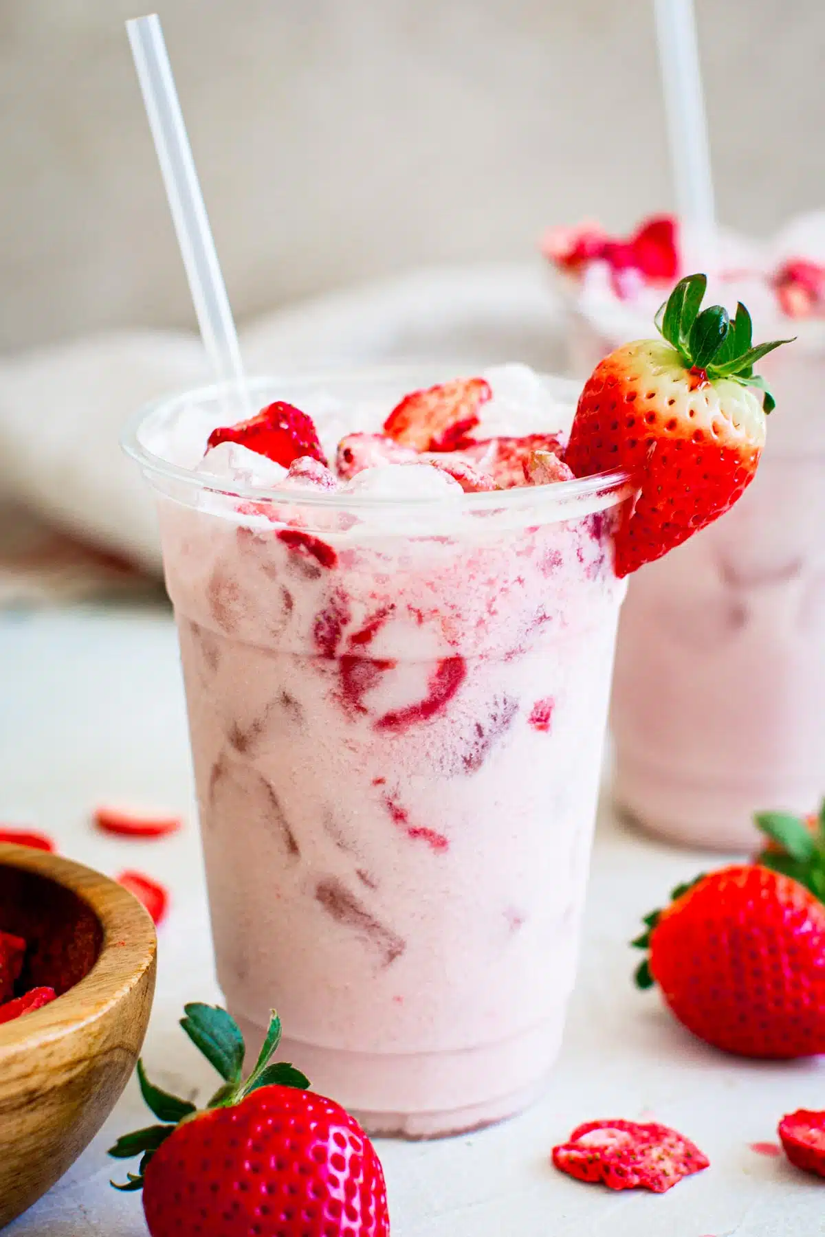 Pink drink in a plastic cup with a straw and strawberry for garnish.