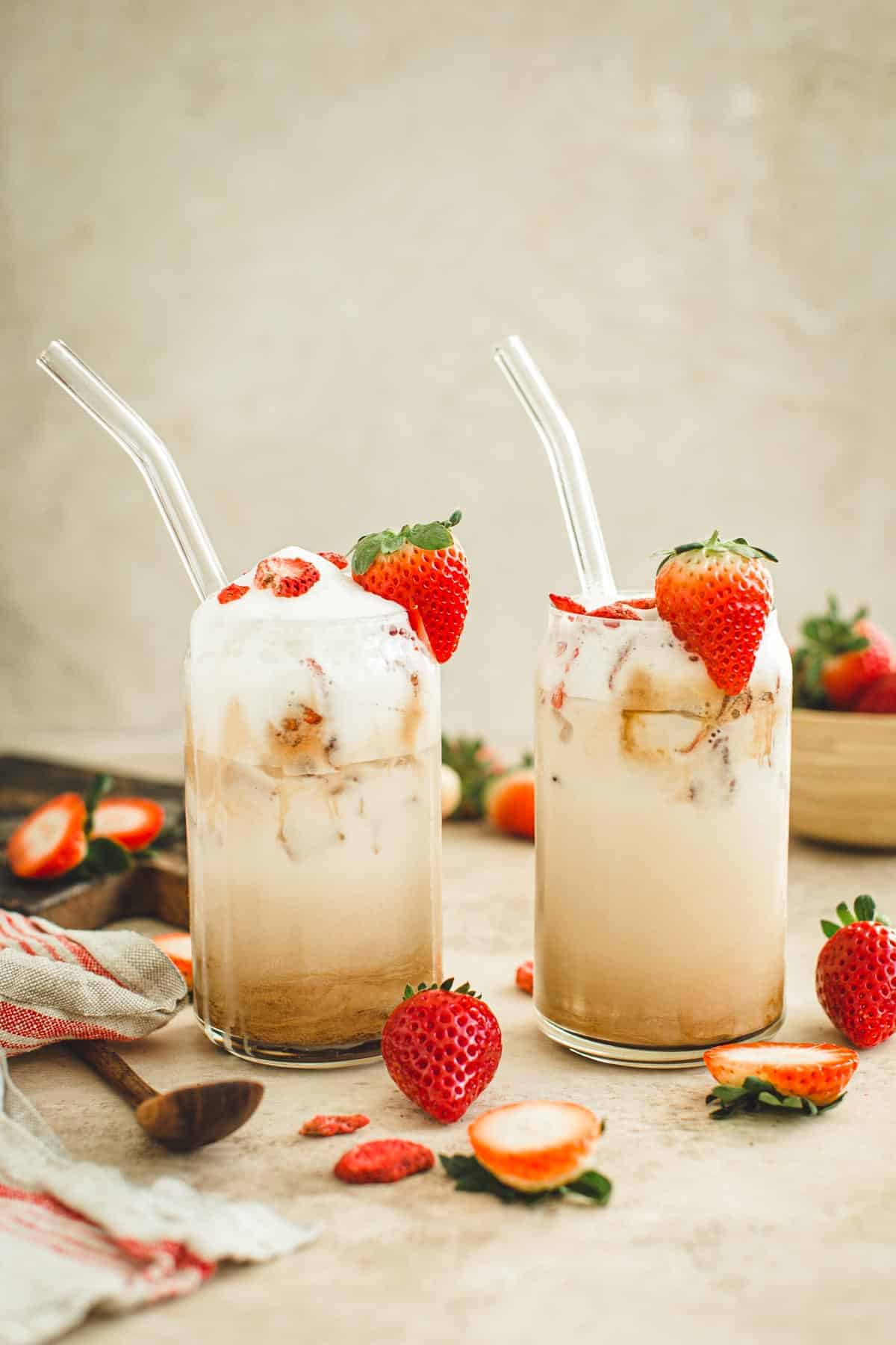 Iced strawberry lattes with a strawberry for garnish on the rim.