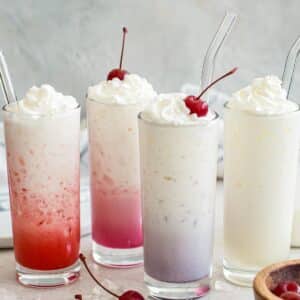 Four different colored Italian sodas topped with whipped cream.