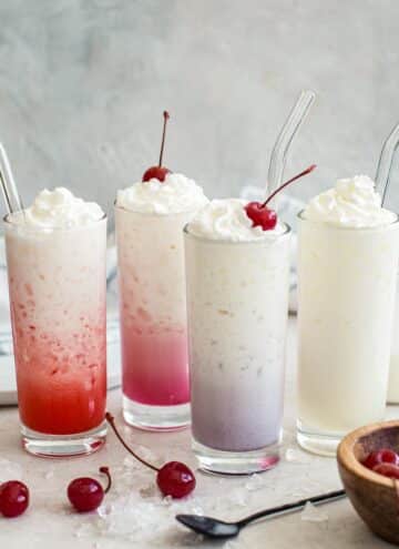 Four different colored Italian sodas topped with whipped cream.
