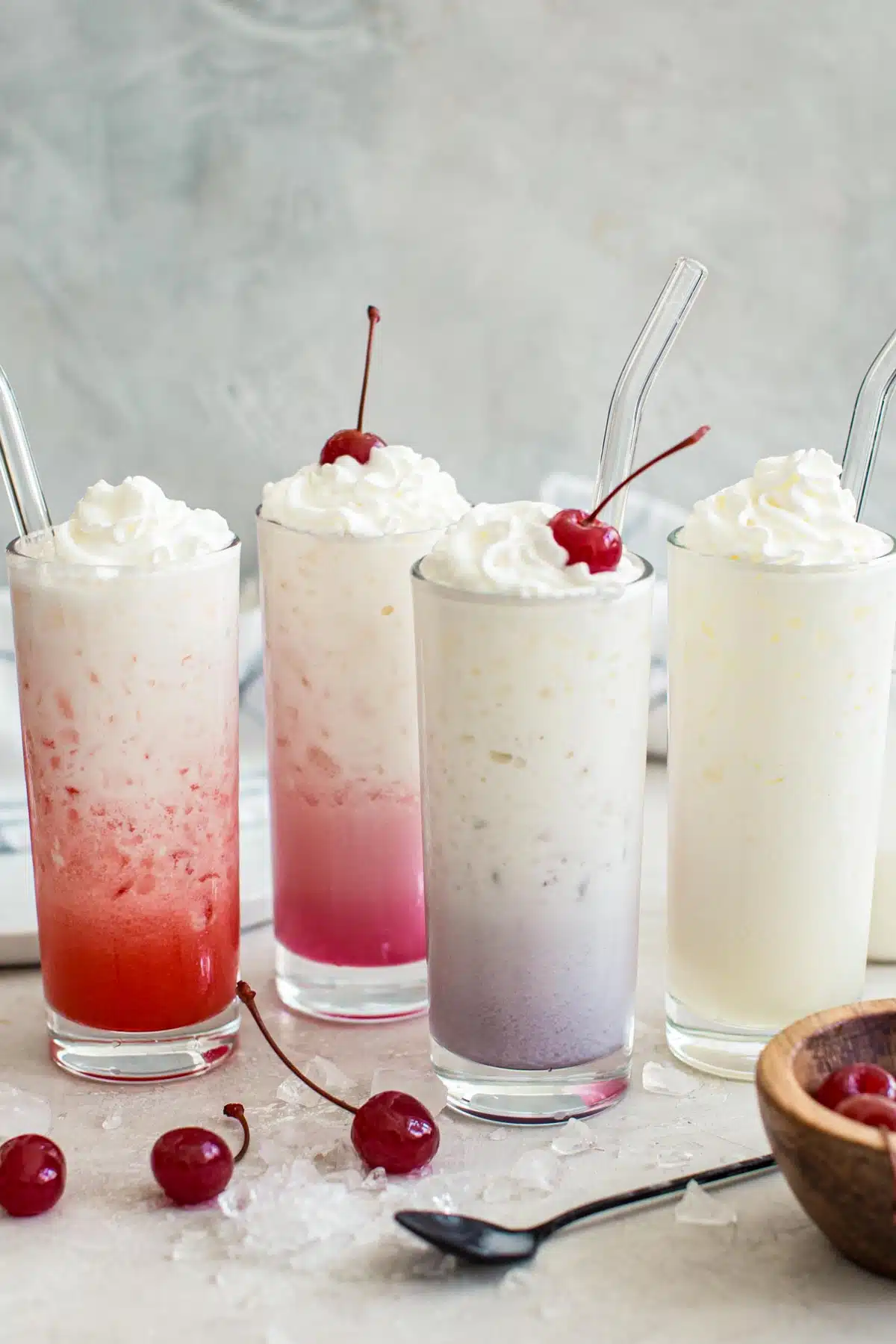 Four different colored Italian sodas topped with whipped cream.