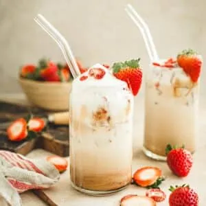 Strawberry latte in a tall glass with a strawberry on the rim for garnish.