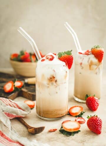 Strawberry latte in a tall glass with a strawberry on the rim for garnish.