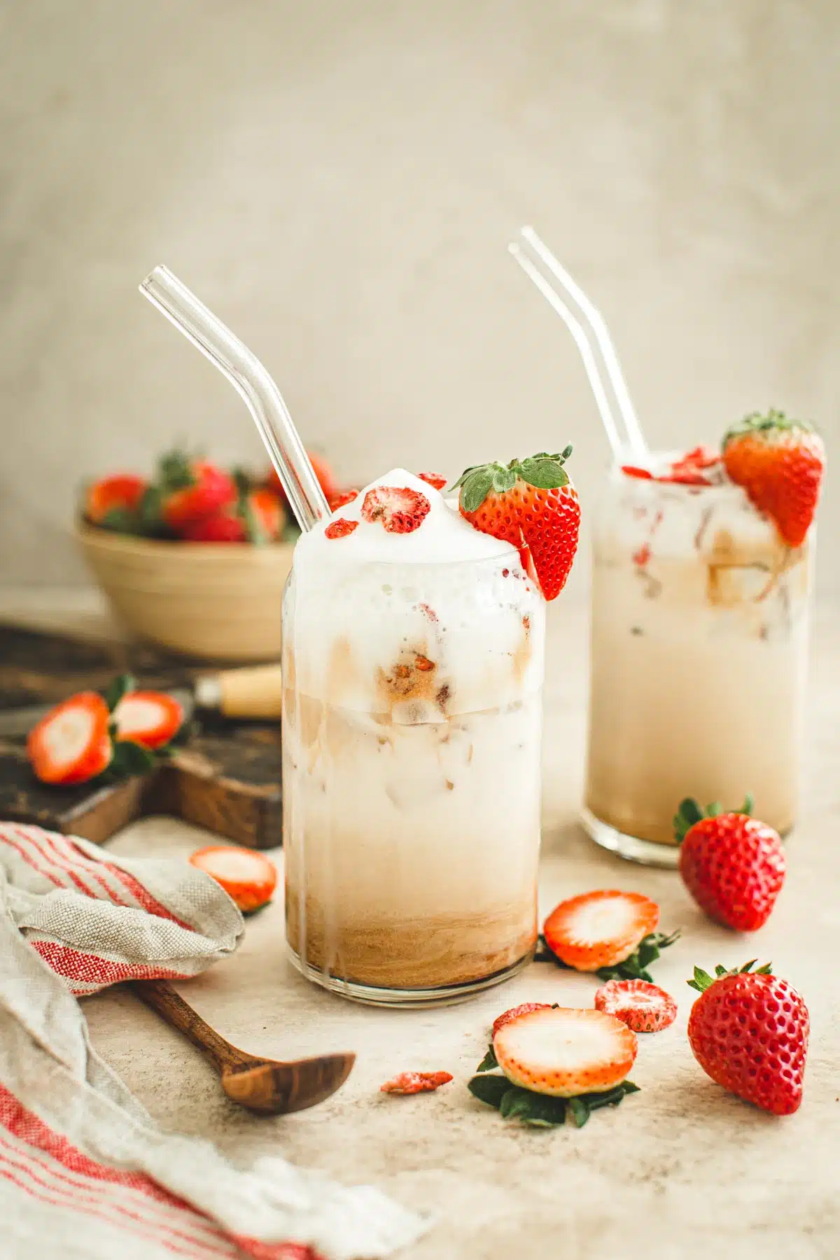 Strawberry latte in a tall glass with a strawberry on the rim for garnish.