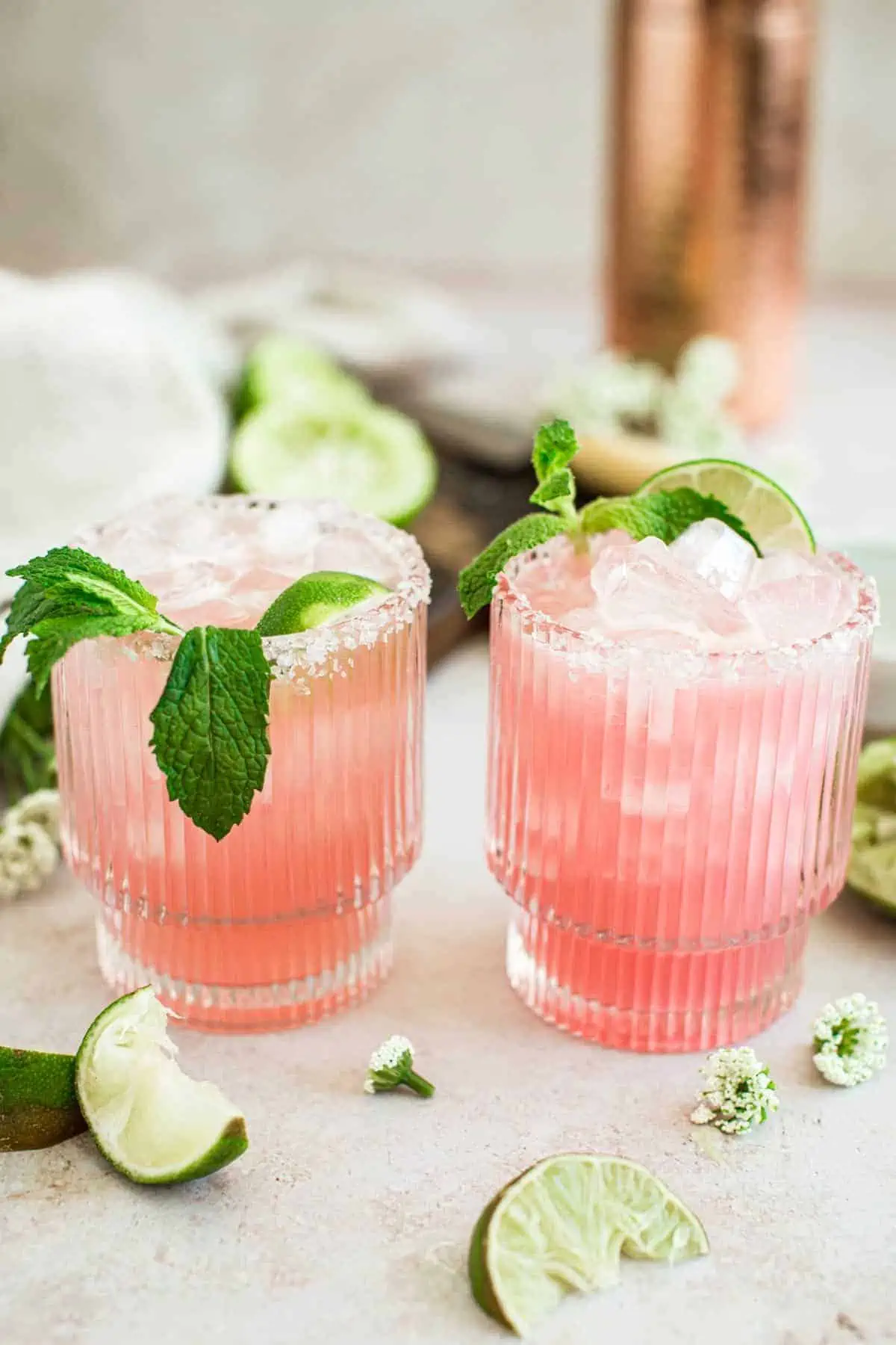 Two pink margaritas topped with mint and limes.