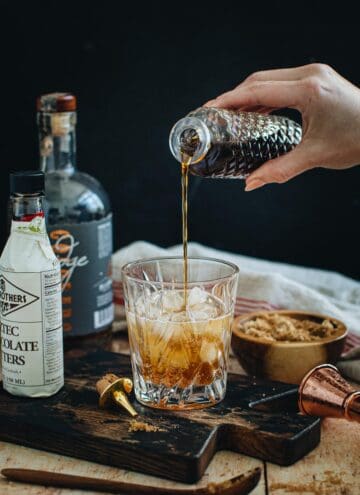 Brown sugar syrup pouring into a cocktail glass with ice.